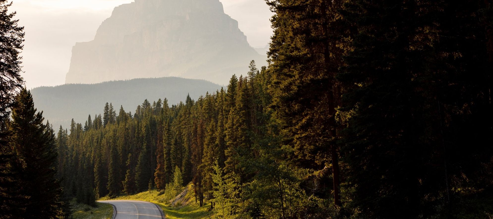 A Jeep drives down the Bow Valley Parkway in Banff National Park with Castle Mountain in the background.