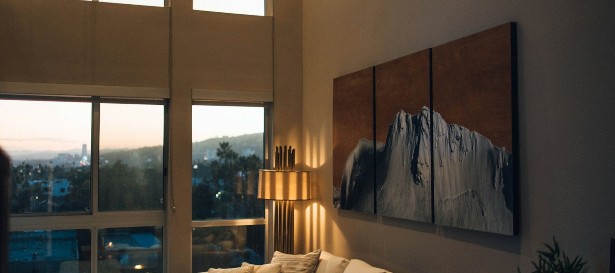 a living room with a white sectional couch, coffee table, and lamp staged in a home for sale with large windows and mountain views