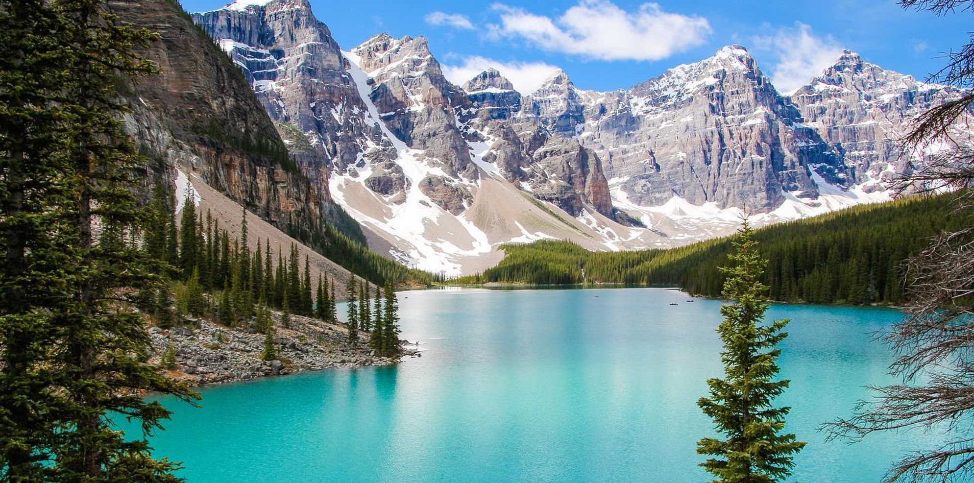 A turquoise lake surrounded by large, snow-capped mountain peaks and tall green trees