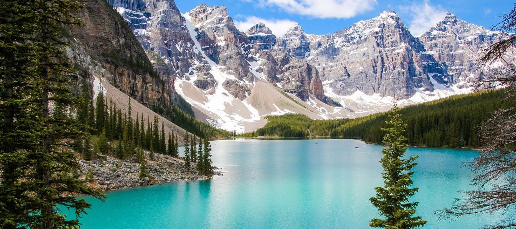 A turquoise lake surrounded by large, snow-capped mountain peaks and tall green trees