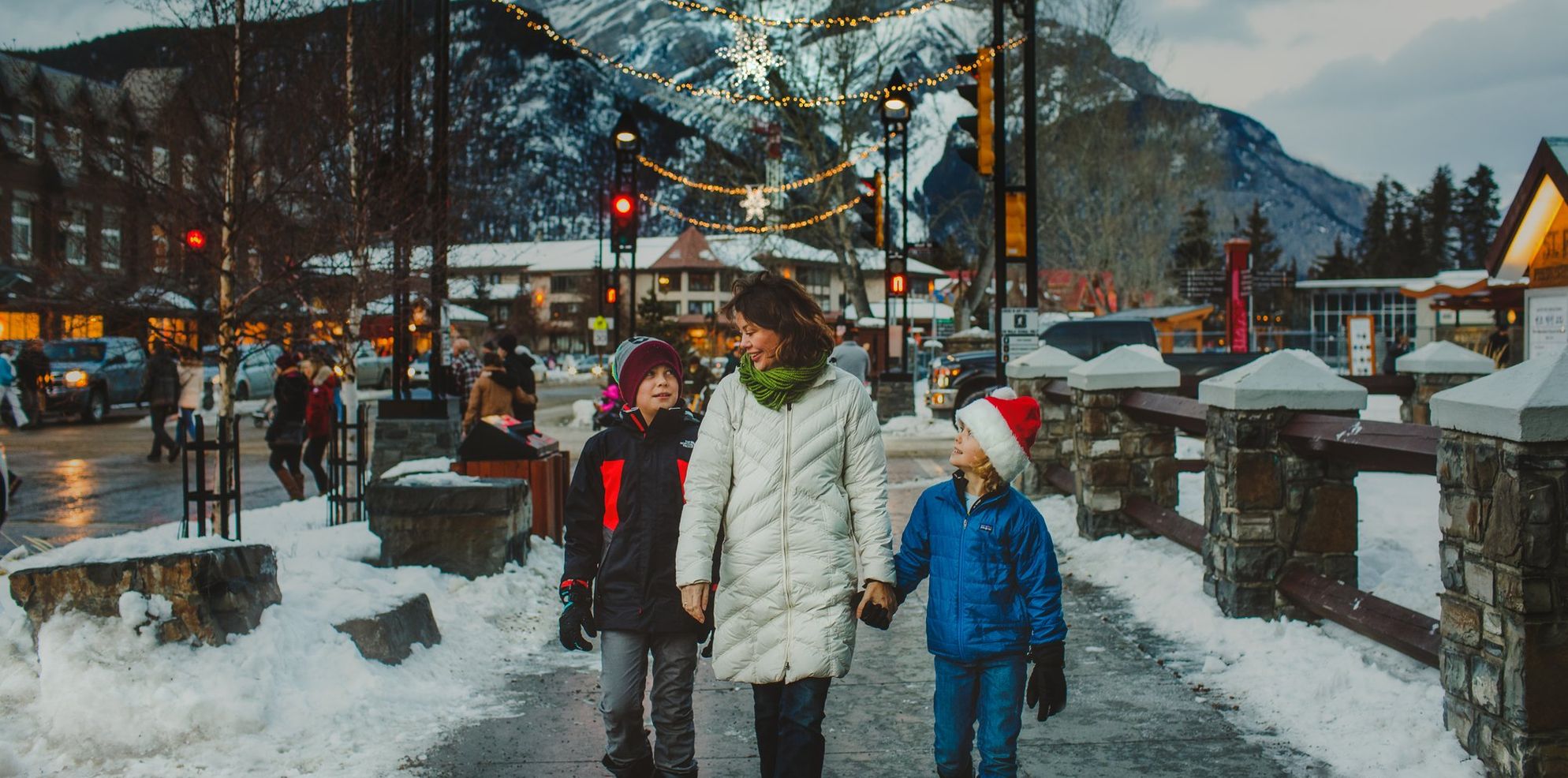 A family walking down Banff Avenue with Christmas lights and mountains behind them