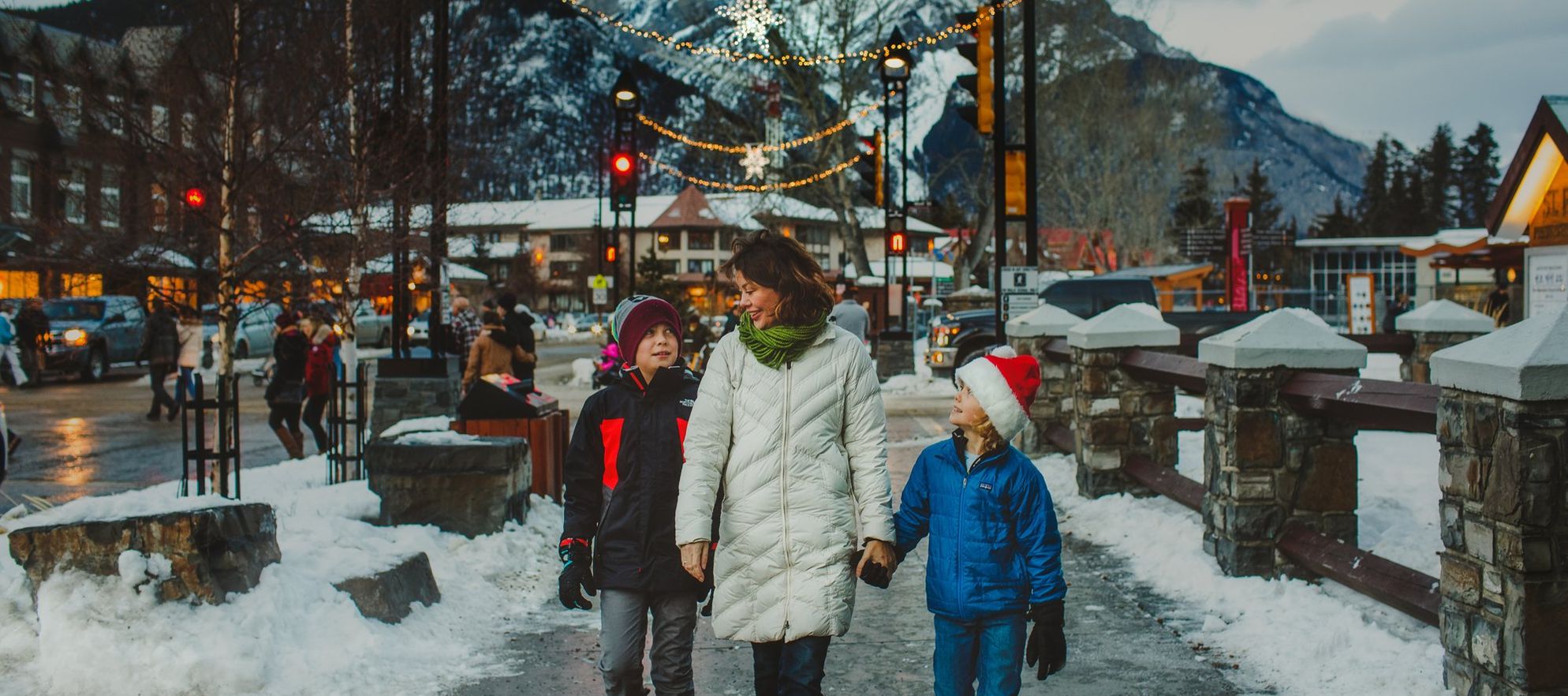 A family walking down Banff Avenue with Christmas lights and mountains behind them