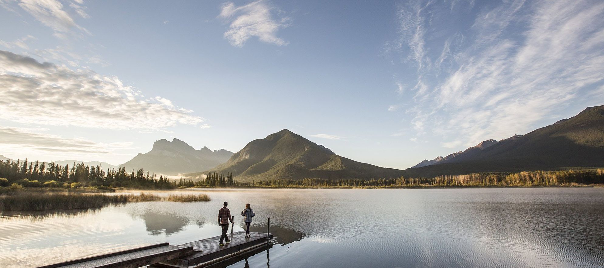 Two people walk onto a dock at Vermilion Lakes in Banff National Park.
