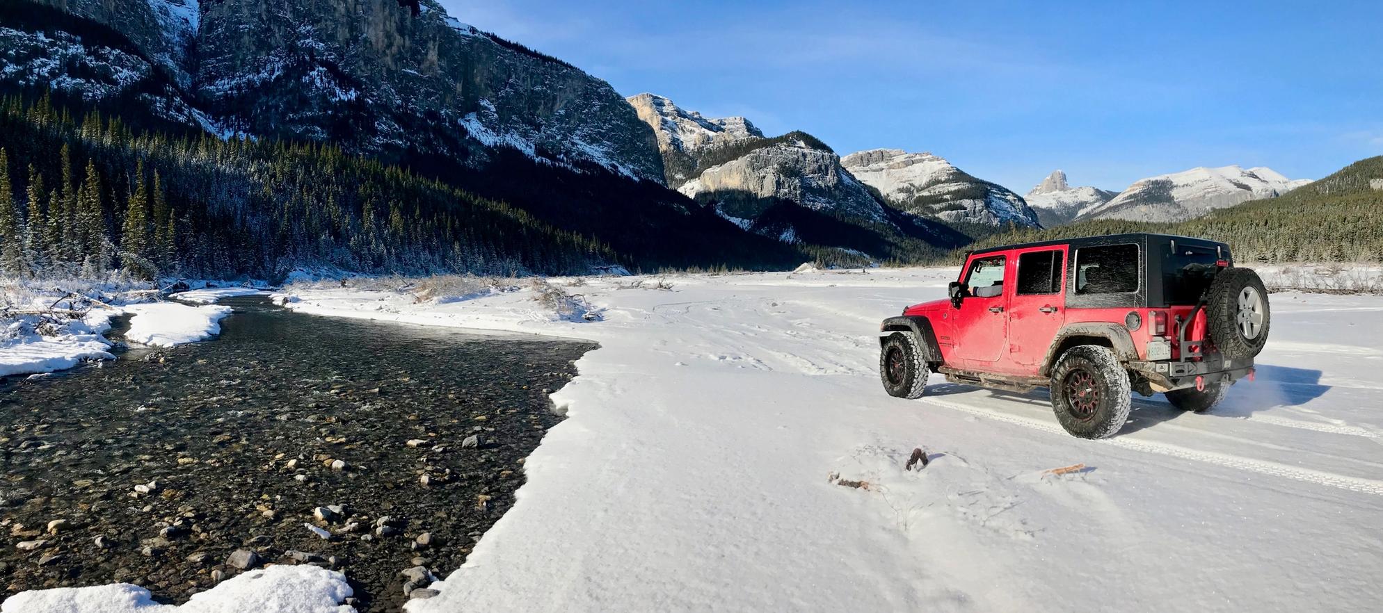 A red jeep off-roading in the backcountry in the winter with mountains in the background