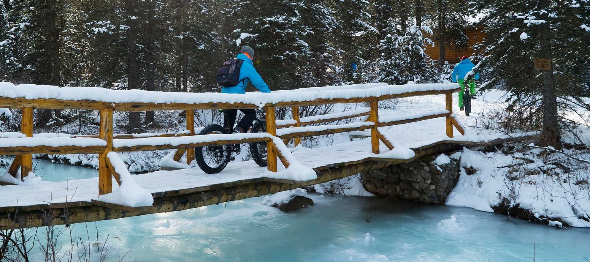 Two friends biking across a snow covered bridge in winter