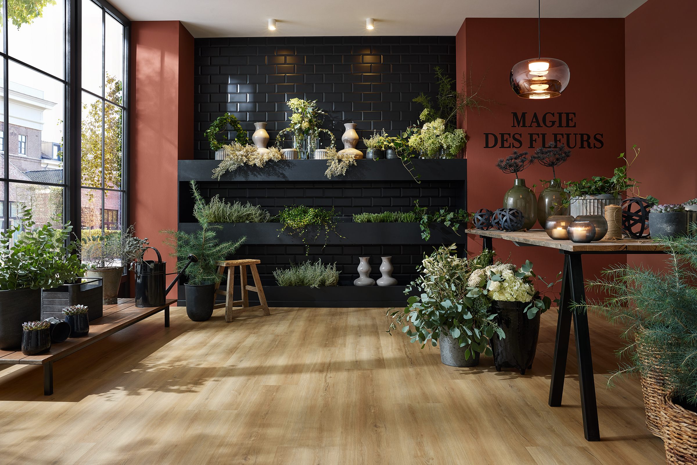 Ein Blumenladen mit dunkler Kachelwand, vielen grünen Pflanzen, eine rostrote Wand und einem tollen Holzboden