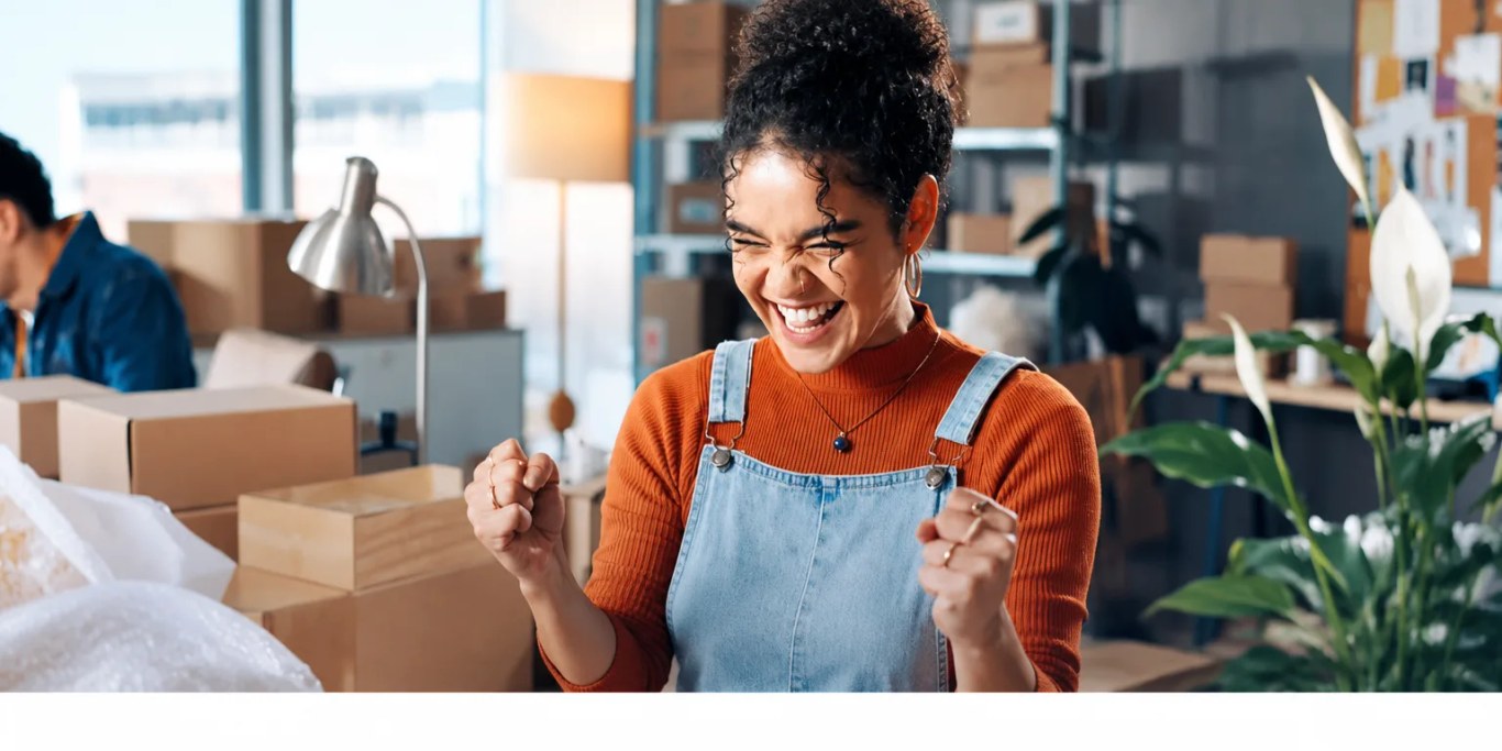 Small business owner celebrating at a laptop surrounded by parcels
