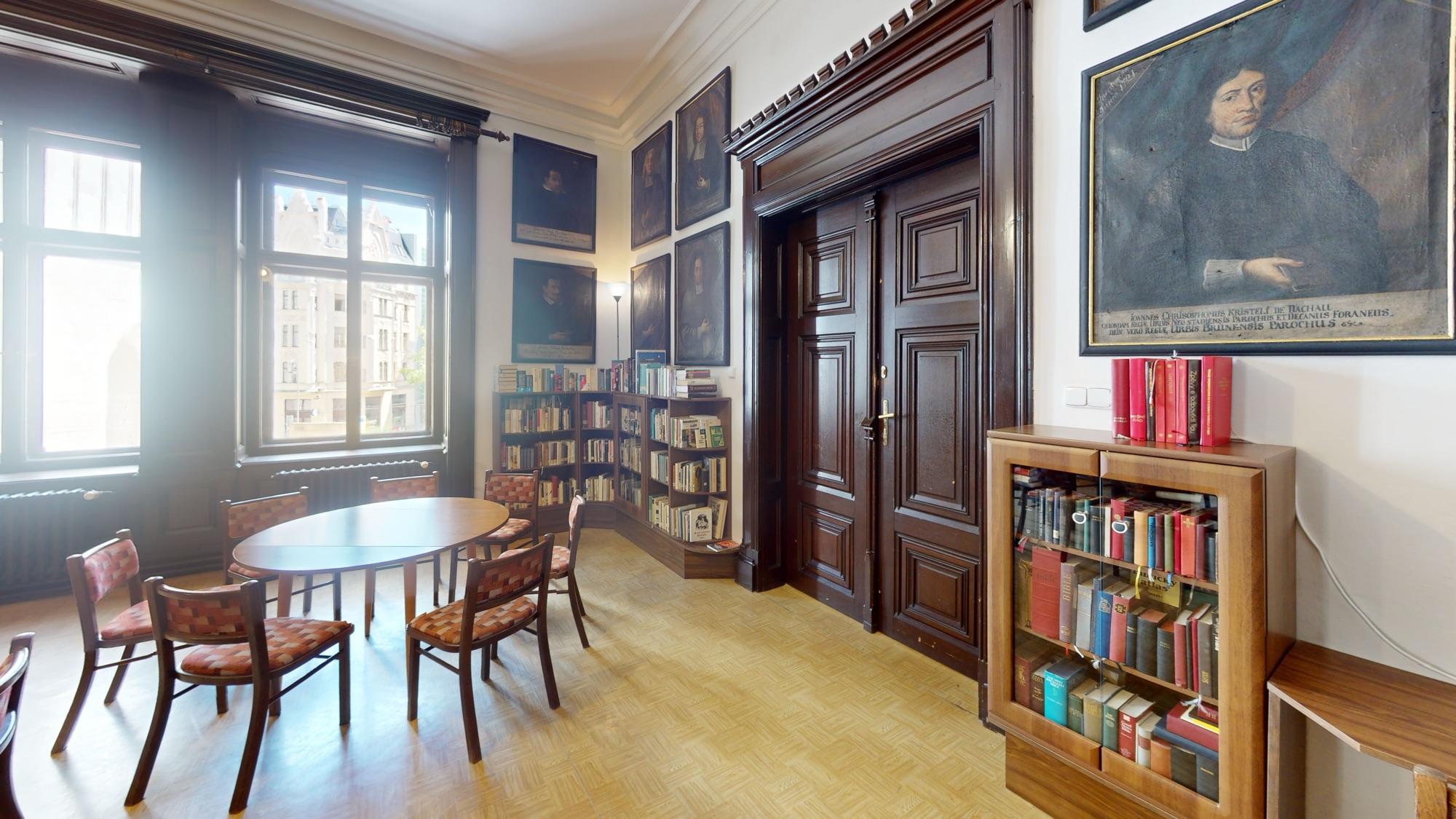 Knihovna s oválným stolem, regály knih a historickými obrazy, Brno