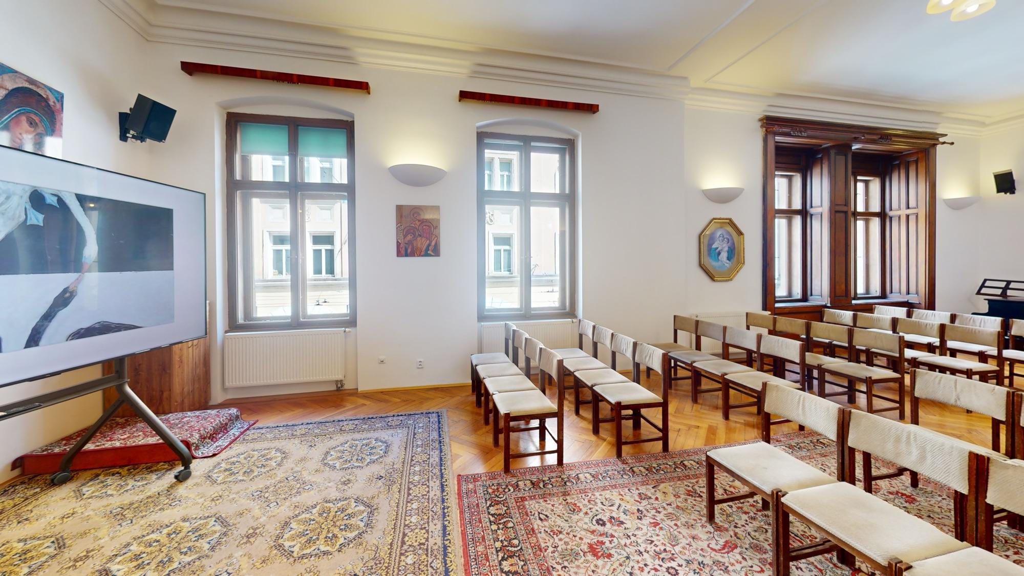Farní sál s řadami židlí a velkou televizí, Brno