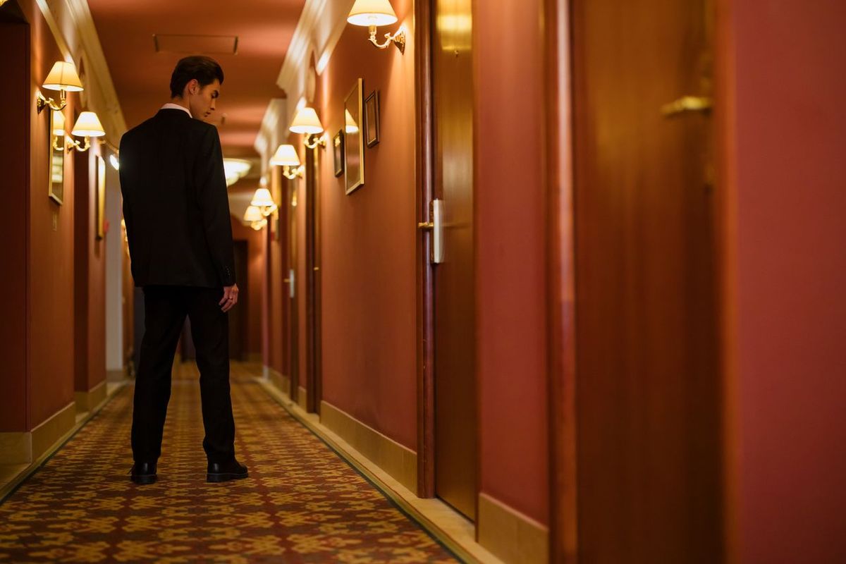 Person in black suit standing in hotel hallway.