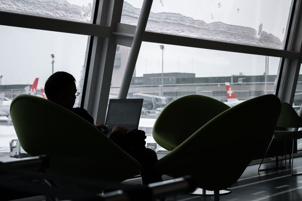 Traveler in airport lounge, working on laptop.