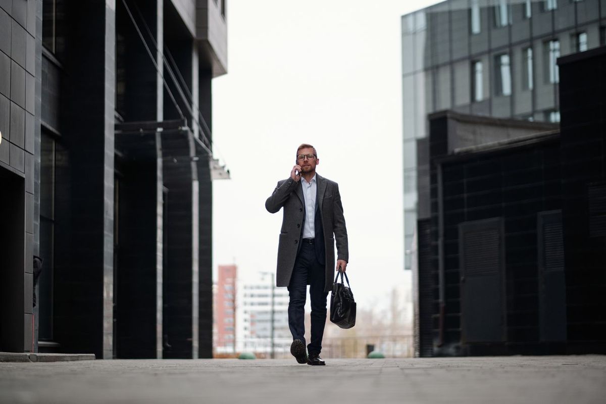 Person in gray coat walking with phone and bag.