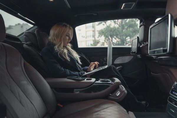 Person working on a laptop in the back seat of a luxury car.