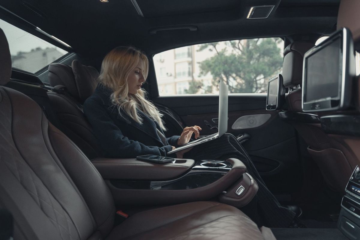 Person working on a laptop in the back seat of a luxury car.