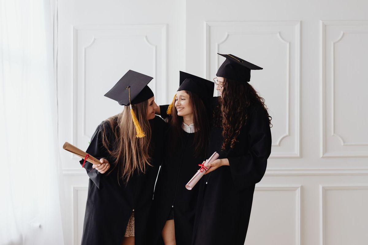 Graduates in caps and gowns holding diplomas and posing together.