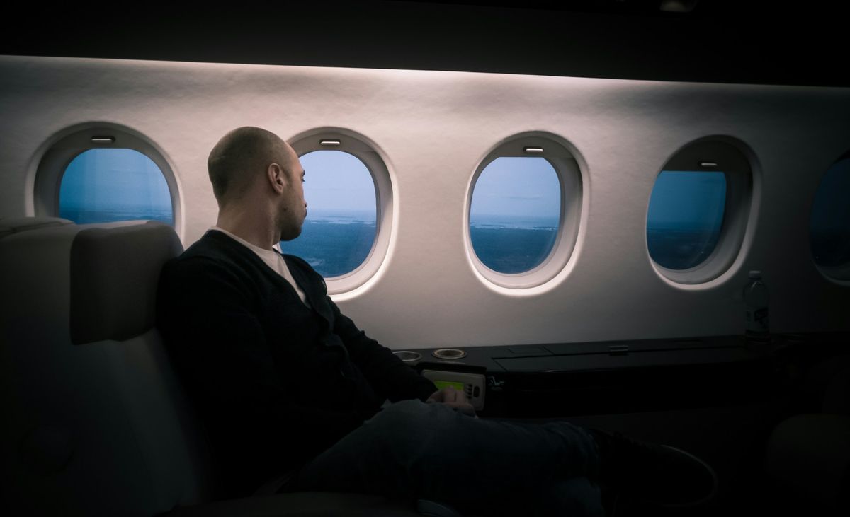 Passenger seated in airplane cabin looking out window.