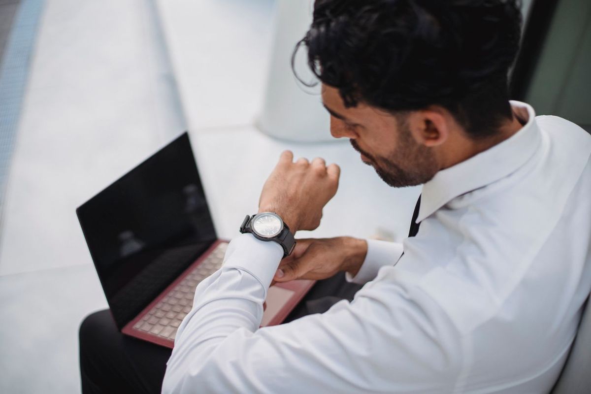 Man in white shirt with laptop checking watch.