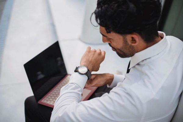 Man in white shirt with laptop checking watch.