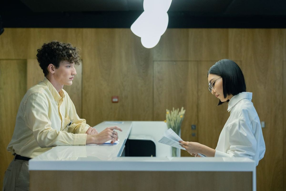 Two people at office counter, reviewing documents in modern reception area.