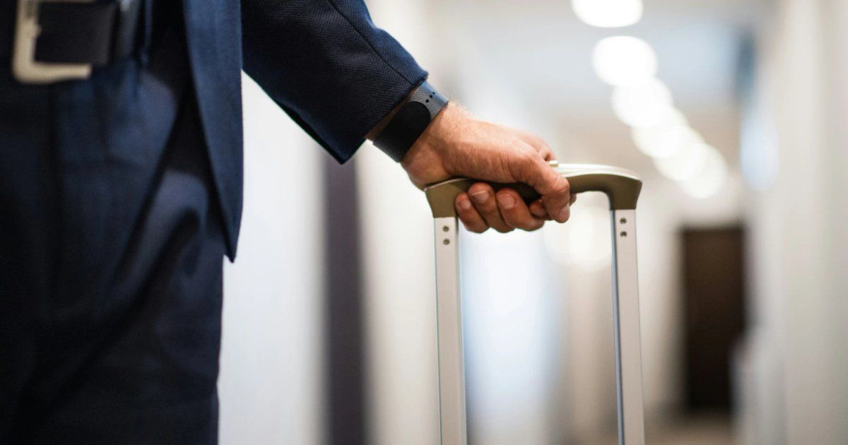 A business traveler in a suit walking a hotel hallway while pulling a rolling suitcase