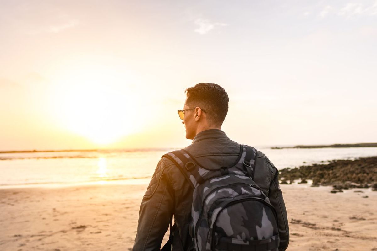 Back view of a man with a backpack enjoying a sunset on a beach