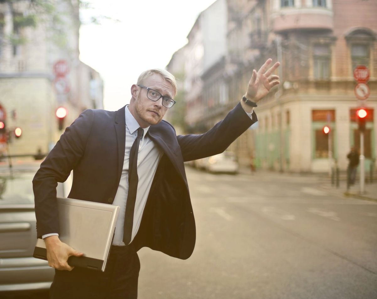 Business professional holding a laptop and hailing a ride on a city street.