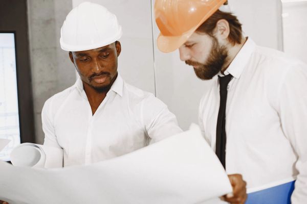 Two engineers in helmets reviewing construction blueprints.