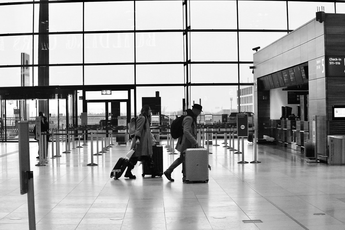 Two travelers with suitcases walking through airport check-in area.