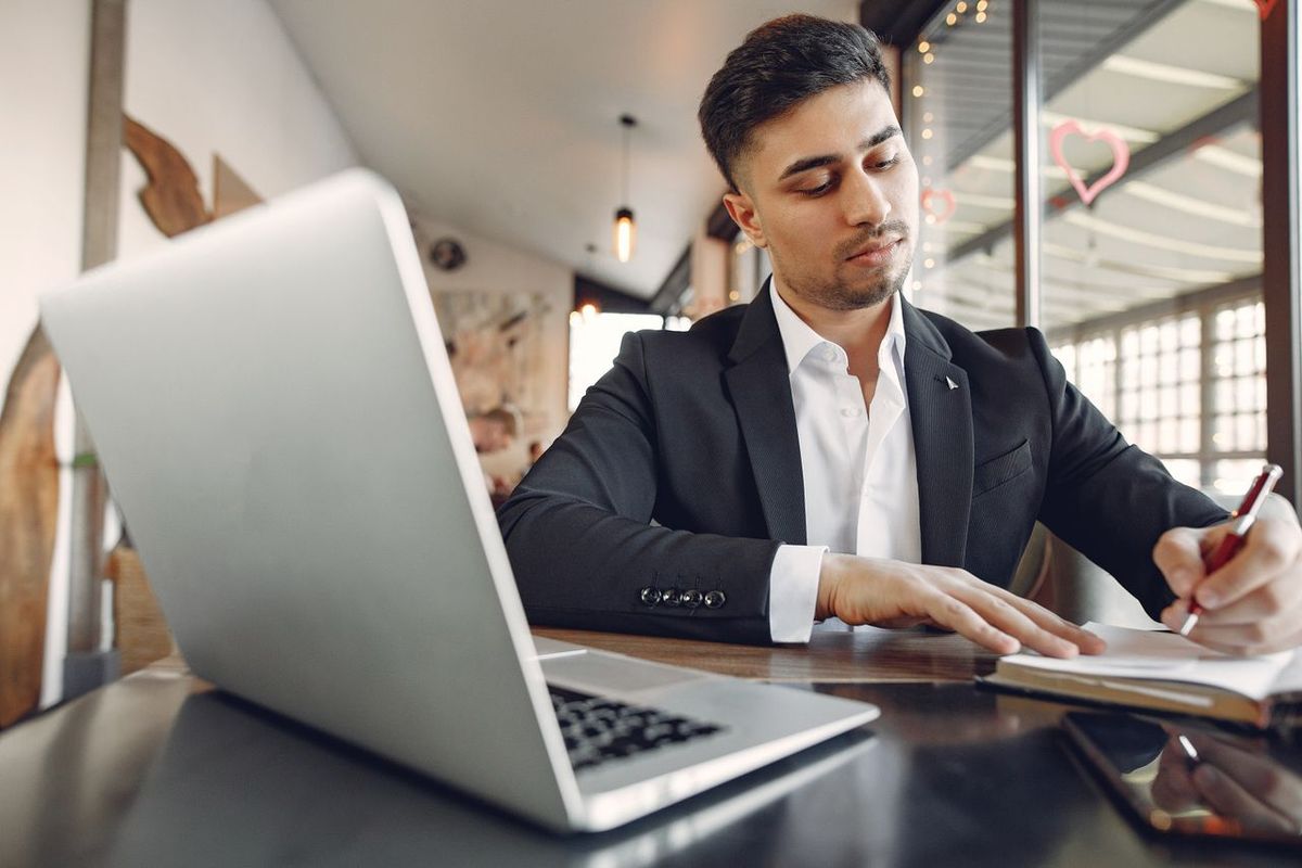 Professional working on a laptop and taking notes at a cafe table.
