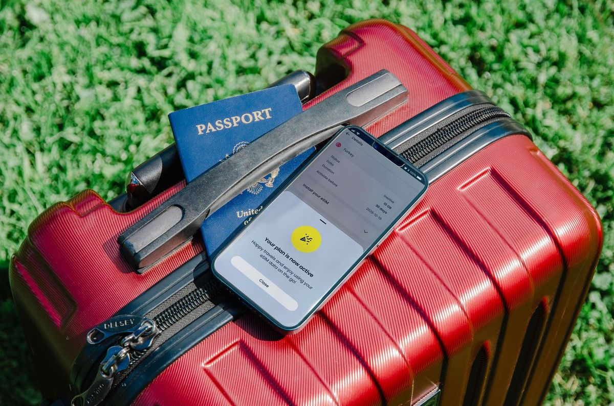 Red suitcase on grass with passport and smartphone.