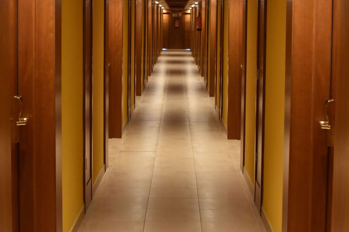 A hotel corridor lined with a row of identical guest-room doors, the physical form of a block of rooms
