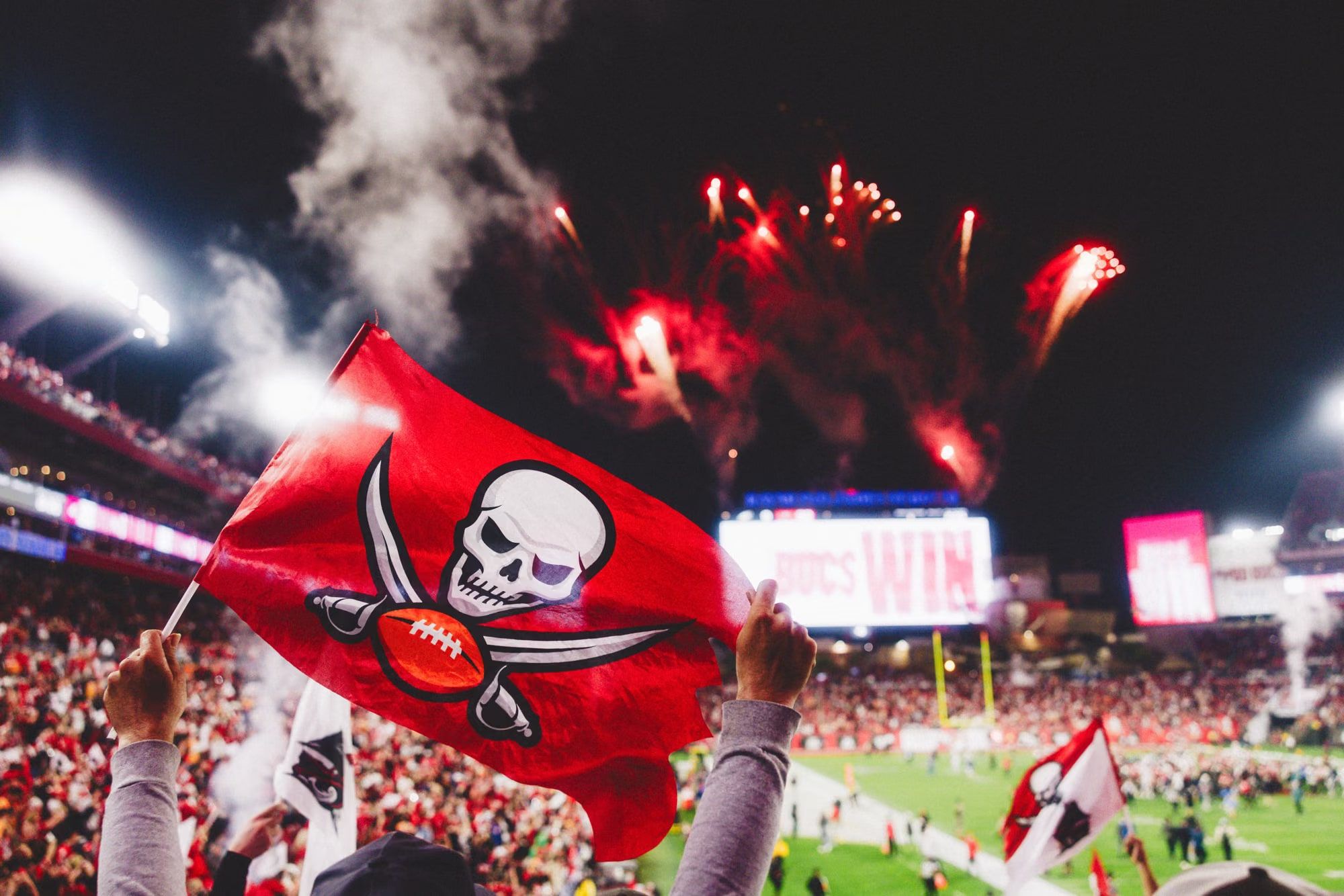Buccaneers fans celebrating with a Jolly Roger flag as fireworks go off over Raymond James Stadium