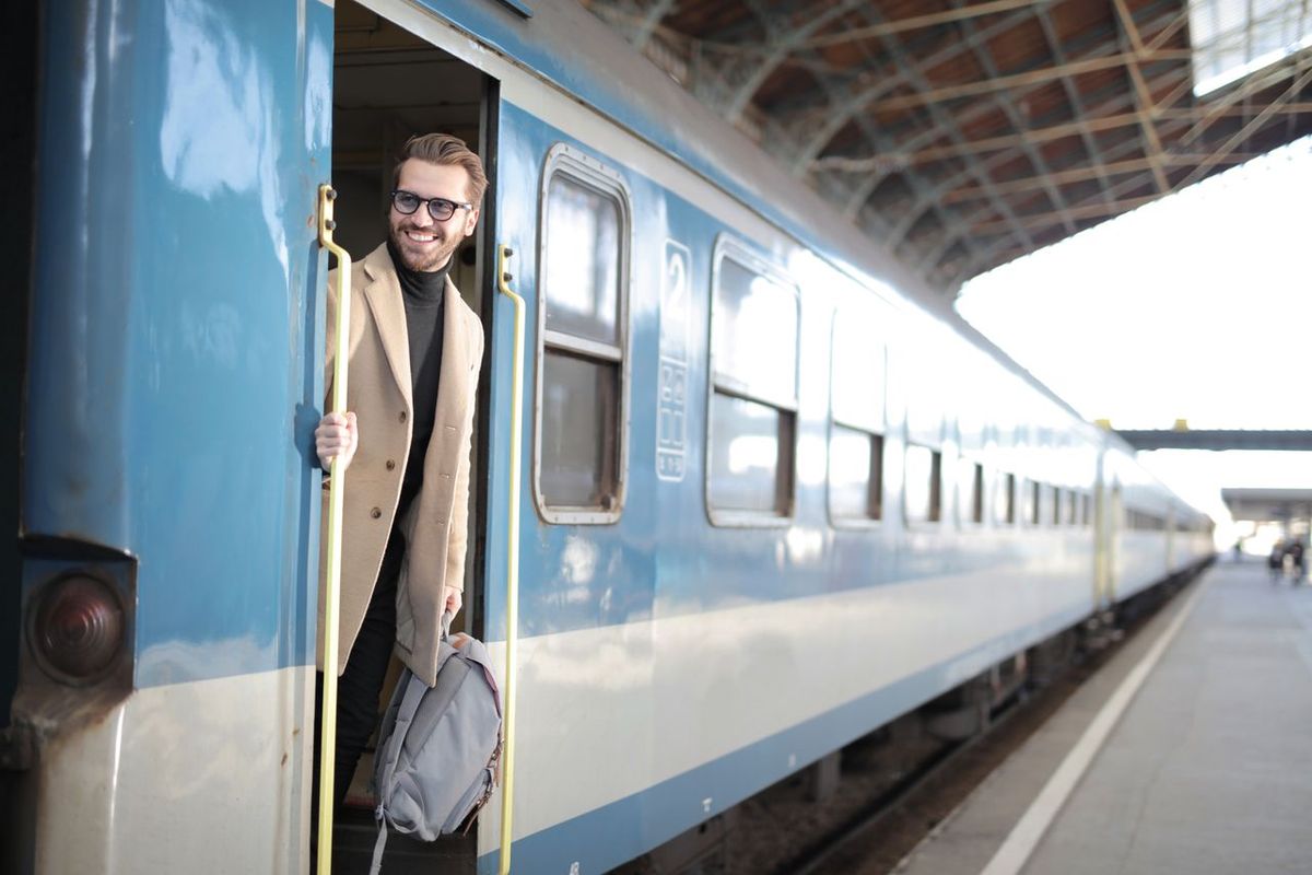 Person stepping out of a blue train at a station platform, carrying a backpack.
