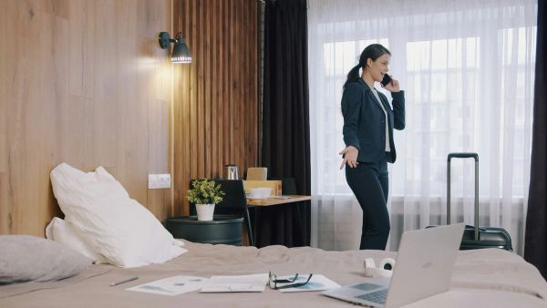 Business traveler in hotel room, talking on phone near suitcase.