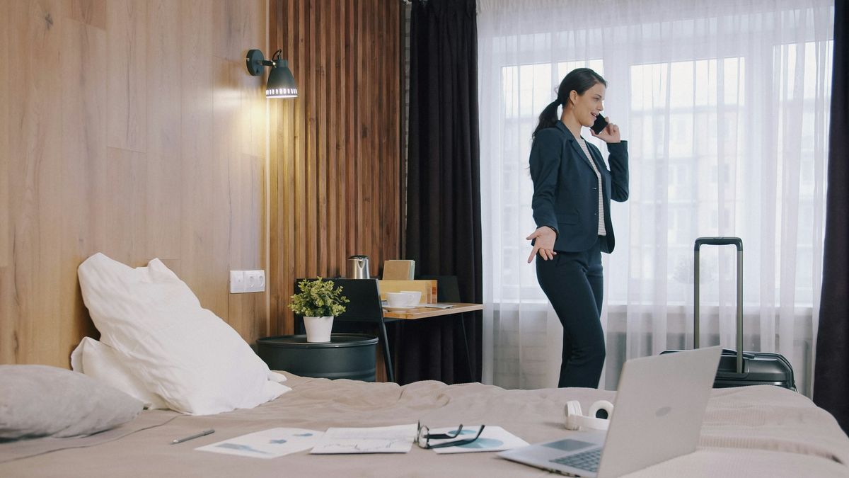 Business traveler in hotel room, talking on phone near suitcase.