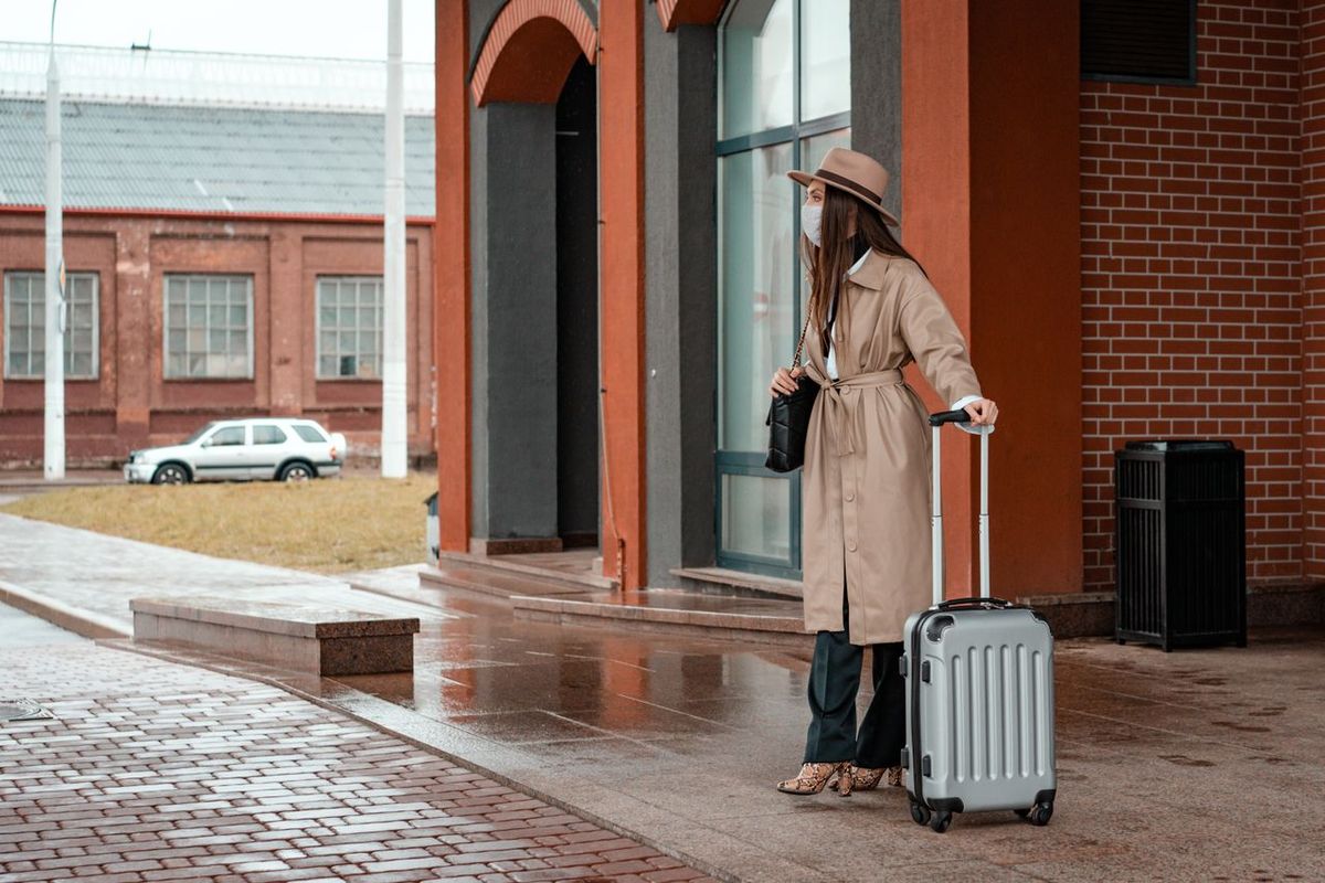 Traveler with a rolling suitcase standing outside a building on a rainy day.