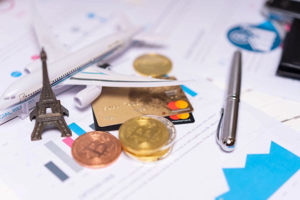 A travel finance concept featuring cryptocurrency, credit card, airplane model, and Eiffel Tower on financial documents.