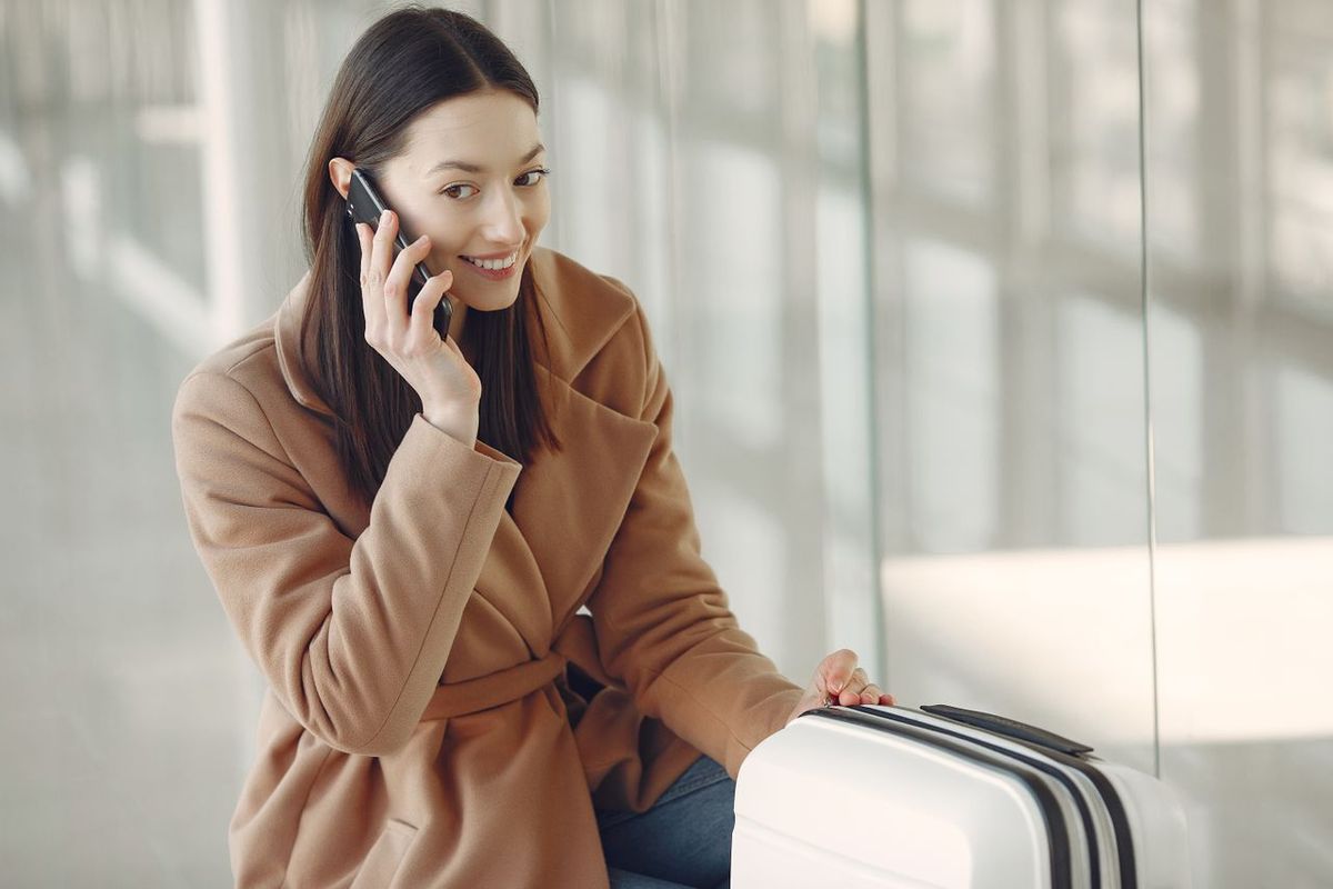 Traveler with a suitcase talking on a smartphone in an airport terminal.