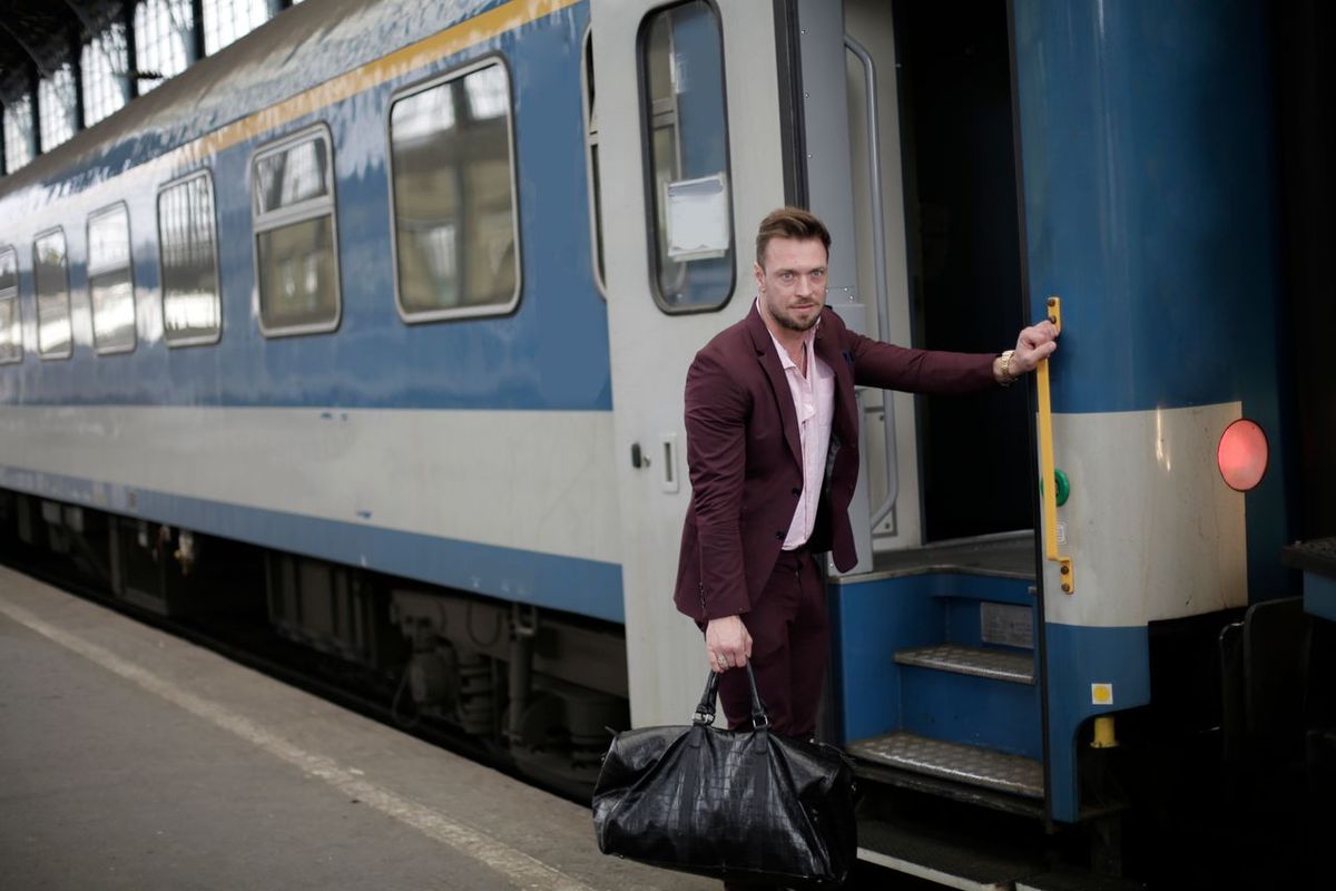 Person with a travel bag stepping off a passenger train at a station.