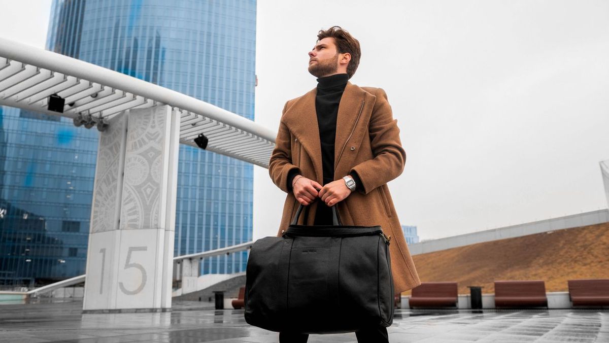 Fashionable man in coat holding a duffel bag.