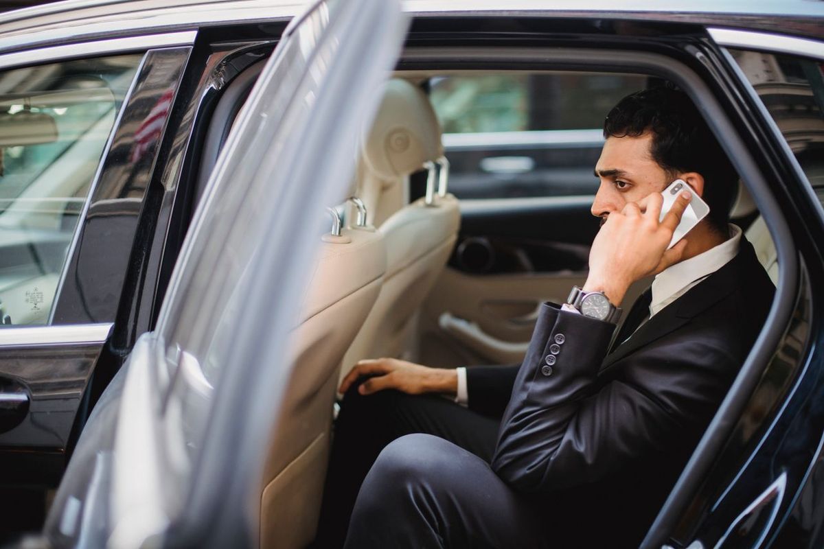 Professional in car with smartphone, engaged in phone call.