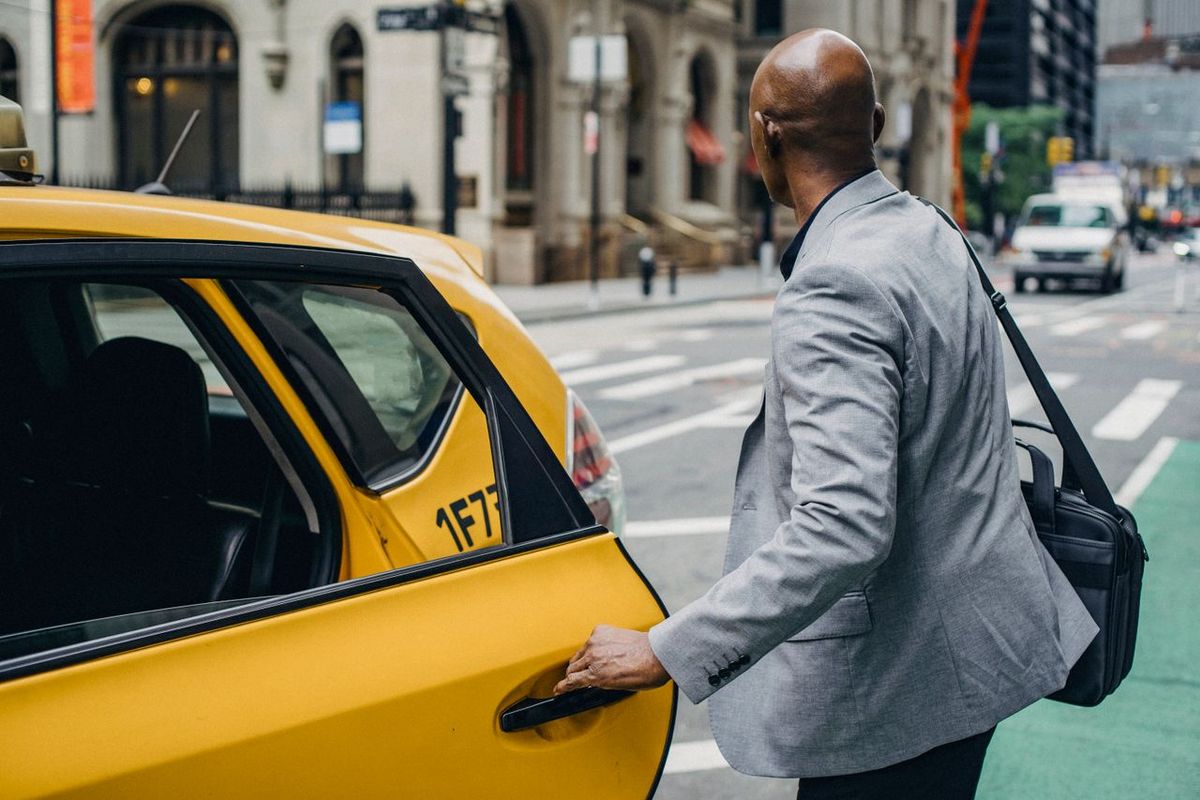 A businessman in a gray suit opens the door of a yellow taxi.