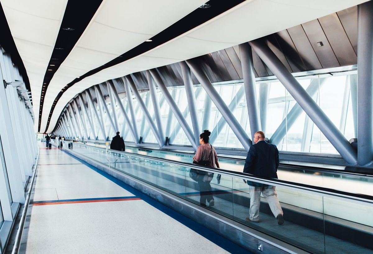 Modern airport walkway with glass panels, sleek ceiling, and travelers on moving walkway.