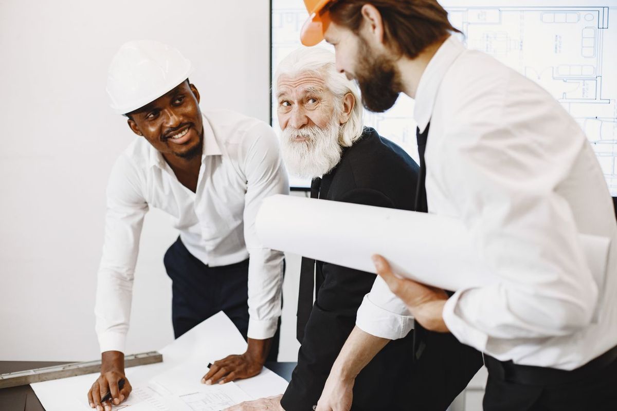 Alt text: Three people reviewing architectural blueprints with safety helmets.