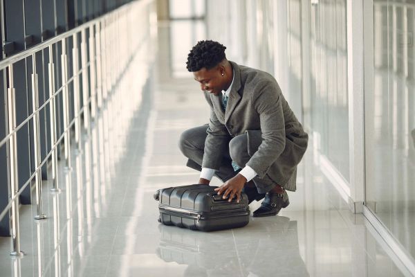 Person in gray suit crouching with suitcase in hallway.