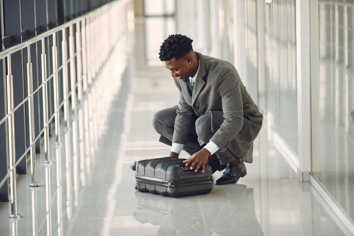 Person in gray suit crouching with suitcase in hallway.