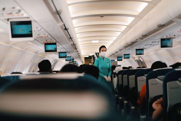 Flight attendant wearing a face mask attending to passengers in an airplane cabin.