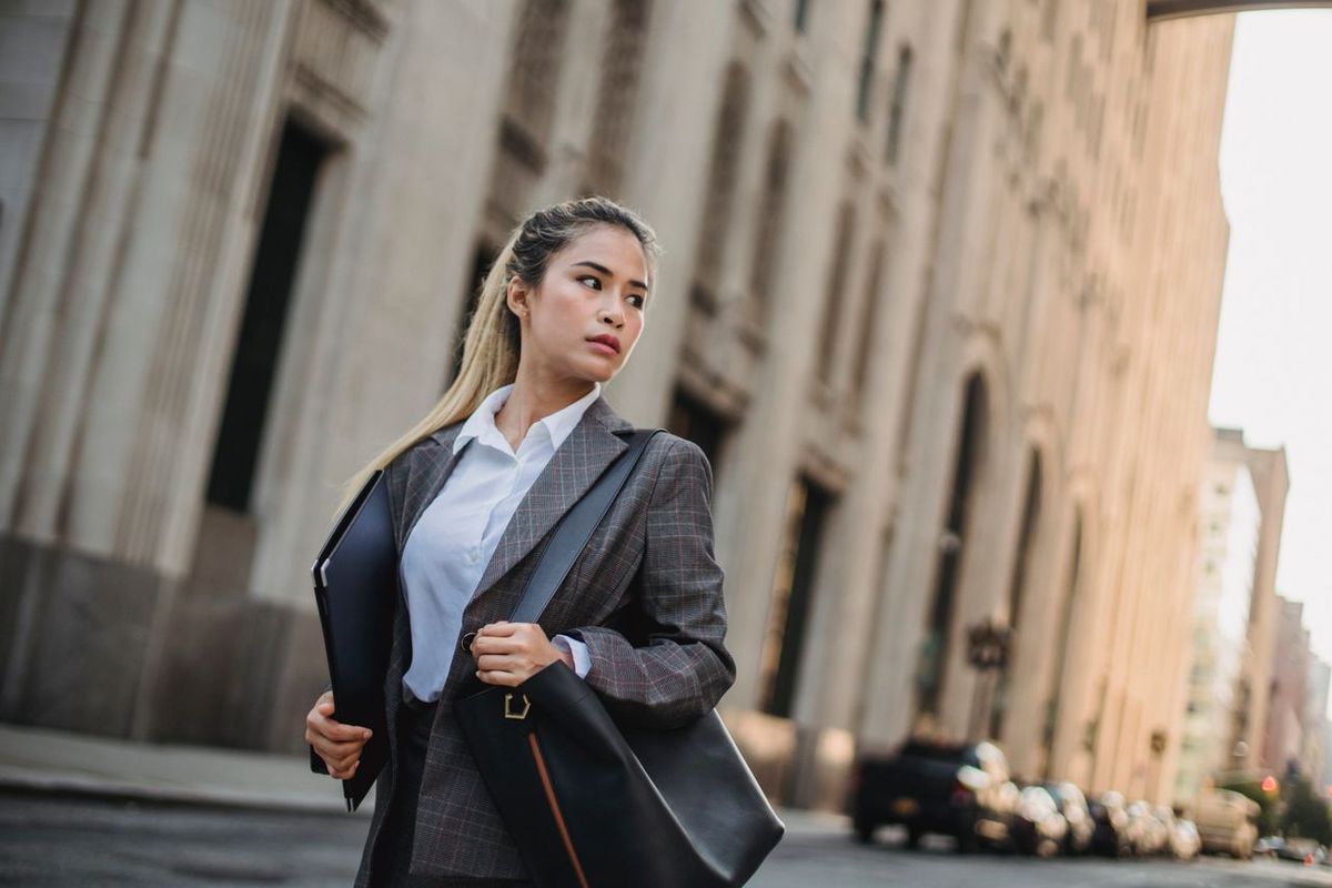Professional carrying a laptop and shoulder bag while walking on a city street.