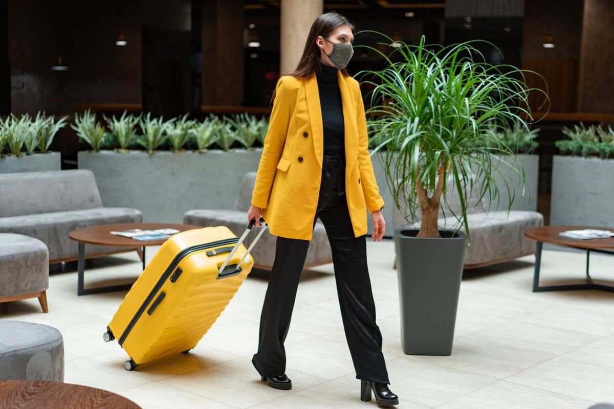 Traveler in yellow blazer pulling suitcase indoors.