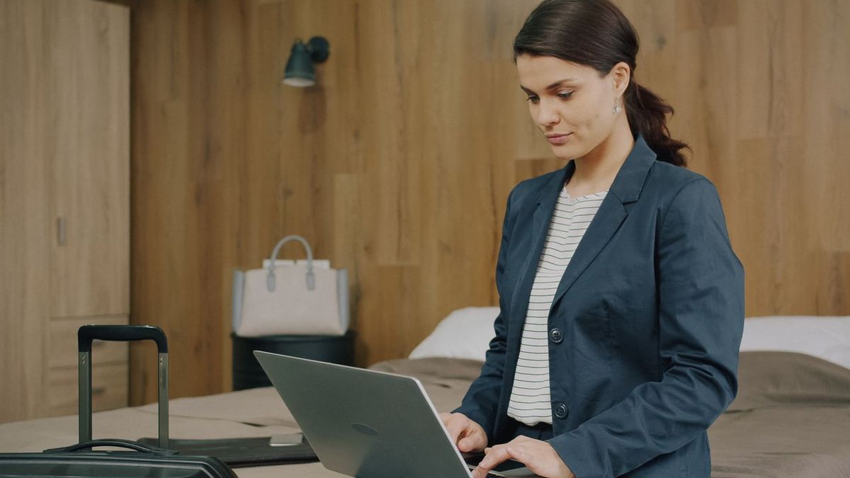 Person in blazer working on laptop in hotel room.